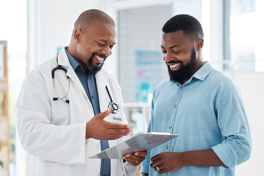 Male medical professional holding a clipboard is in conversation with male patient