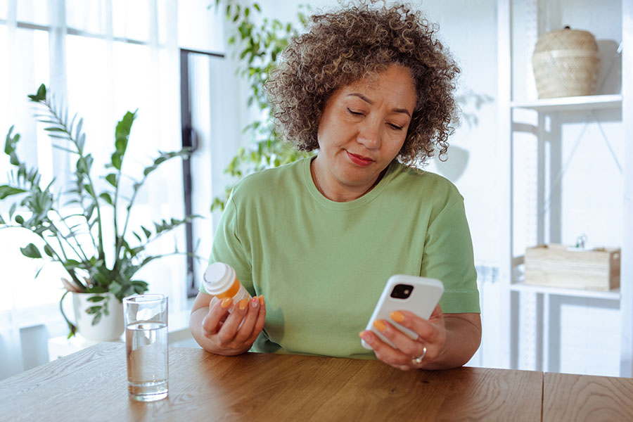 Adult female is holding a prescription bottle while viewing information on her mobile device