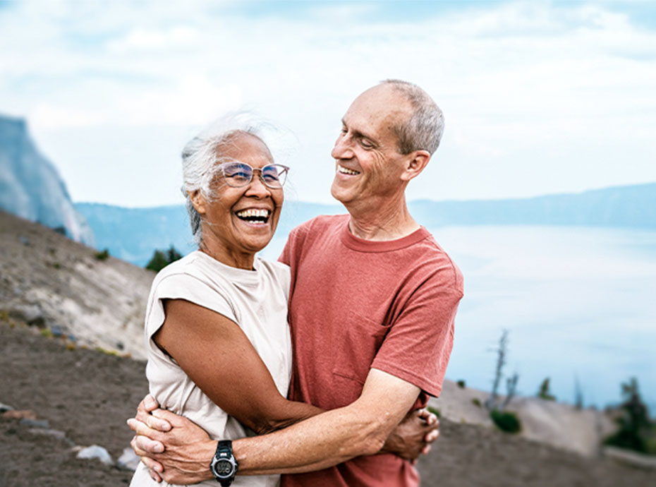 Older couple hugging and smiling outdoors near water and mountains